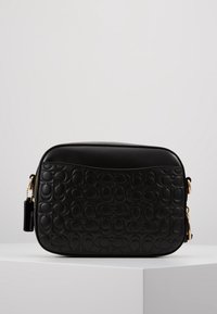 Musta nahkainen olkalaukku, jossa on kohokuvioitu logokuvio, sileä pinta, kultaiset metallikoristeet ja vetoketjusuljenta. Kompakti suorakulmainen muoto.