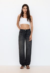 Fekete farmerszéles nadrág fehér gyöngyökkel díszítve; magas derék és klasszikus öt zsebes kialakítás; fehér crop top-pal viselve.
