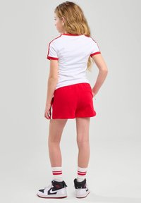 Pantalones cortos rojos con una parte de arriba blanca que presenta acentos rojos. Tejido blanco con ribetes rojos, diseño deportivo y ajuste casual. Combinados con zapatillas altas.