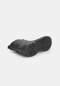 Botina din piele neagră cu o talpă robustă și un model de profil unic. Are un mic maner de tragere și o suprafață texturată, concepută pentru durabilitate.