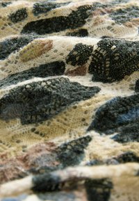Patroon kantstof met verschillende donkergroene en bruine vormen op een crèmekleurige achtergrond, met ingewikkelde texturen en een delicate uitstraling.