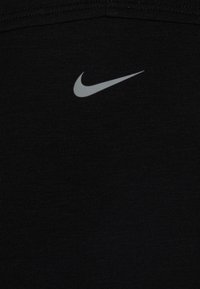 Juodas sportinis marškinėlis, pagamintas iš minkštos medžiagos, su pilku "Nike" ženkliuku, centruotu krūtinėje, ir paprastu, moderniu dizainu.