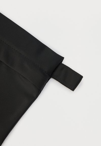 Μαύρη γωνία υφάσματος με ραμμένη θηλιά, πιθανότατα μέρος μιας τσάντας ή θήκης, εμφανιζόμενη σε απλό ανοιχτό φόντο.