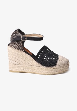 Juodas pintas espadrilės stiliaus platformos sandalas su natūralios jūtos platforma, turi kulkšnies dirželį, atvirą pirštą ir tekstūruotą makramė viršutinę dalį.