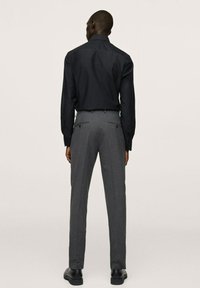 Schwarzes Langarmshirt kombiniert mit grauen, tailiertes Hosen. Das Shirt hat eine glatte Textur, während die Hose ein dezentes Muster aufweist.