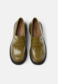 Green leather loafers with a rounded toe, featuring a stitched design and a black rubber sole. Interior lining showcases the brand name.