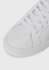 Sneaker in pelle bianca con lacci bianchi piatti, punta arrotondata, cuciture tonali, suola in gomma testurizzata e finitura liscia sulla tomaia.