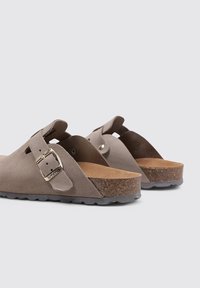 Gray suede slip-on sandals with a cork footbed, featuring a metallic buckle and a textured rubber sole. Open back design.