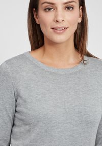 Lys grå genser med rund hals og strikket tekstur, med en tettsittende design og en glatt finish.
