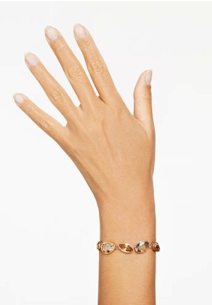 Bracelet en or présentant des pierres précieuses de forme ovale aux couleurs claires et ambrées, reliées par des montures métalliques délicates, porté sur une main.