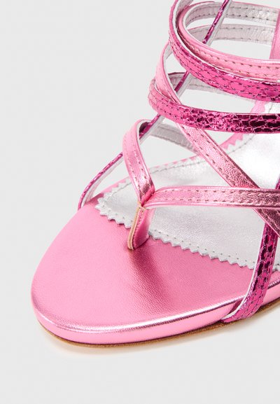 Rozā metāla strappy sandaļi ar pirkstu cilpu, teksturētām potīšu siksniņām un gaišas sudraba iekšpuses uz balta fona.