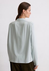 Camicia azzurro chiaro a maniche lunghe con vestibilità comoda, texture morbida e dettagli plissettati discreti nelle cuciture delle spalle.