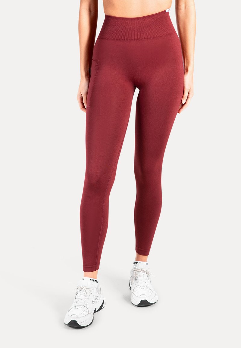 Sportleggings in bordeauxrood, hoog getailleerd ontwerp, rekbare stof, gladde textuur, met zijzakken, gecombineerd met witte sportschoenen.