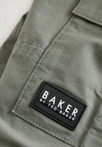 Groene stof met een subtiele, textuurafwerking; bevat een zwart label met de tekst "BAKER BY TED BAKER," dat schone lijnen en naai-details toont.