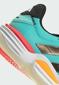 Türkise Sportschuh mit einem Mesh-Obermaterial, schwarzen Akzenten, metallischen Details und kontrastierenden pinken und orangenen Bereichen an der Sohle.