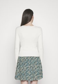 Maglione bianco a coste con maniche lunghe, abbinato a una gonna a fantasia con colori teal, beige e navy. Vista posteriore, sfondo minimalista.