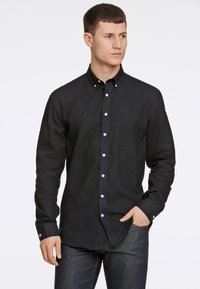 Zwarte button-up shirt gemaakt van textielstof met lange mouwen en witte knopen. Gepaard met donkere denim jeans.