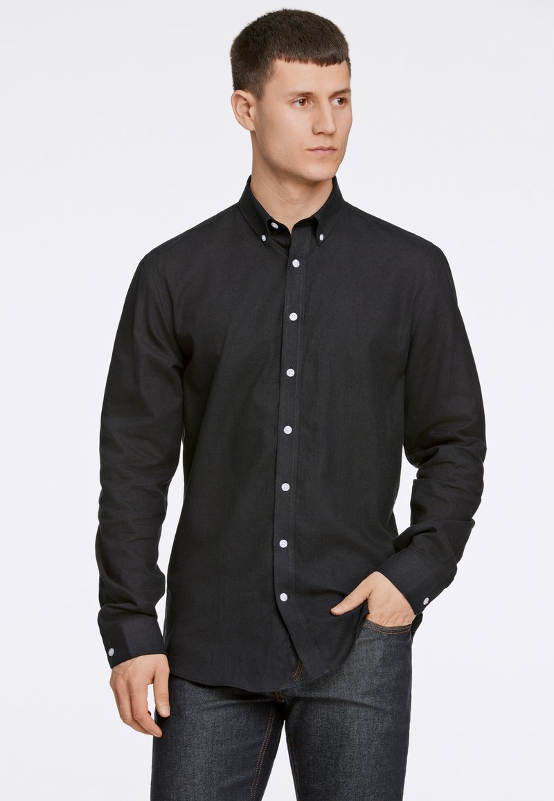 Zwarte button-up shirt gemaakt van textielstof met lange mouwen en witte knopen. Gepaard met donkere denim jeans.