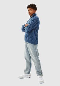 Blå kabelstickad tröja med hög krage, matchad med ljusblå raka jeans och vita sneakers med grå detaljer.