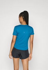 Blaues sportliches T-Shirt mit kurzen Ärmeln, Rundhalsausschnitt und subtilen Logodetails auf dem Rücken. Kombiniert mit schwarzen Sportshorts.