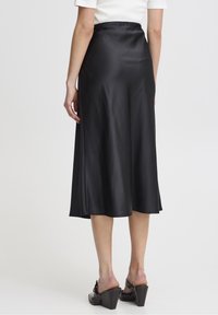 Musta satiininen midi-hame, jossa on sileä rakenne, levenevä muoto ja joustava vyötärö. Yhdistetty avonaisiin korkokenkiin.