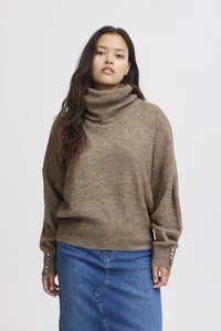 Brun, mjuk stickad tröja med hög polokrage och lös passform. Har texturerat tyg och knapplister på ärmarna. Matchas med en denimkjol.