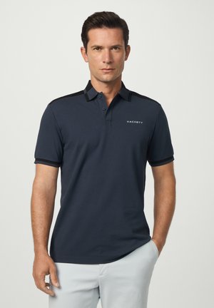 Mørkeblå polo t-shirt med sort krave og ærmer, der har en knappet placket og "HACKETT" logo broderet på brystet. Glat stoftekstur.