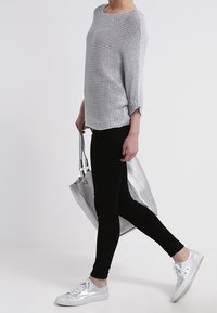 Silberner Strickpullover mit lockerer Passform, schwarze Leggings und metallisch silberne Sneakers. Inklusive einer großen silbernen Handtasche mit strukturierter Oberfläche.