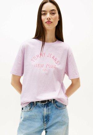 Lyse lilla bomulds t-shirt med "TOMMY JEANS NEW YORK CITY" i røde broderede bogstaver. Korte ærmer og rund halsudskæring. Casual pasform.