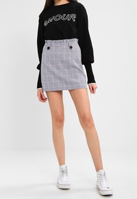 Černá mikina s nápisem "AMOUR" v bílé barvě, kombinovaná s upnutou sukní s kostkovaným vzorem a detaily na stahování a knoflíky. Bílé tenisky.