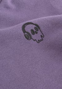 Graphisme d'un crâne noir portant des écouteurs sur un fond en tissu doux, violet, avec une texture tricotée visible.