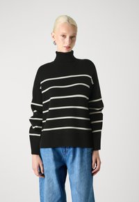 Black and cream striped sweater with a high turtleneck and loose fit, paired with light blue wide-leg jeans. Smooth texture, ribbed cuffs.