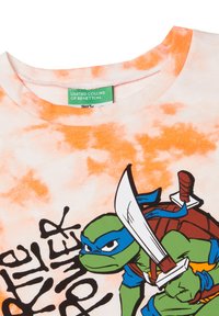 Camiseta con un patrón de tie-dye naranja, que presenta una impresión gráfica de un personaje de tortuga verde sosteniendo una espada y el texto "Poder de Tortuga".