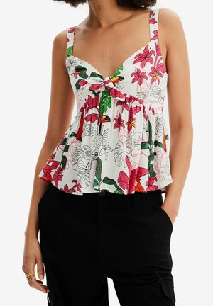 Mujer con top blanco sin mangas con estampado tropical de flores rosas y verdes y tucanes, combinado con pantalones negros.
