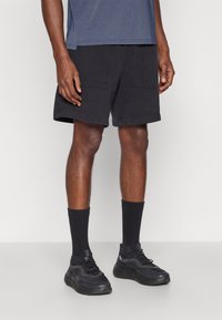 Calções cargo pretos com bolsos, combinados com meias de tornozelo pretas e sapatilhas. A parte de cima é uma t-shirt azul de manga curta.