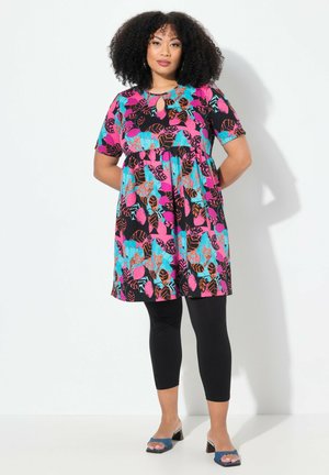 Abito colorato con una base nera, caratterizzato da vivaci motivi a foglia in rosa e teal. Abbinato a leggings neri e sandali con tacco blu.