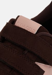 Braune Wildledersneaker mit einem pinken Lederstab. Enthält Klettverschluss-Riemen und detaillierte Nähte. Branding auf dem Stab sichtbar.