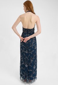 Mørkeblå aftenkjole med halterneck, perlede blomster mønstre og en tætsiddende overdel, der flyder ud til en gennemsigtig frynset kant.