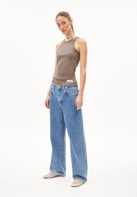 Sleeveless brown tank top, blue baggy jeans, light-colored shoes. Notable details include a ribbed texture and a logo on the tank.