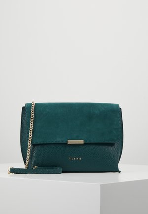 Donkergroene Ted Baker leren crossbodytas met suède klep en gouden kettingriem, tentoongesteld op een wit oppervlak.