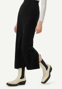 Pantalons larges en maille côtelée noire associés à des bottines beiges à la cheville avec des panneaux latéraux noirs et un talon épais.