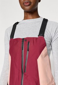 Červeno-ružový s kapucňou s dvojitým zipsom, nastaviteľnými čiernymi popruhmi a ľahkou textúrou, s farebne blokovanými panelmi.