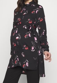 Svart gravidblus med mönster av rosa och röda blommor, långa ärmar, knäppkrage och band i midjan. Mjuk, lätt tyg.