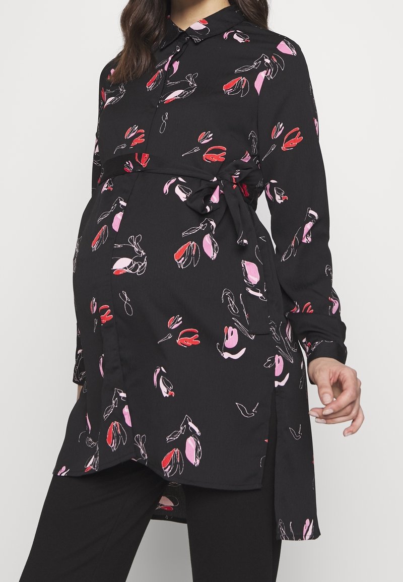 Svart gravidblus med mönster av rosa och röda blommor, långa ärmar, knäppkrage och band i midjan. Mjuk, lätt tyg.