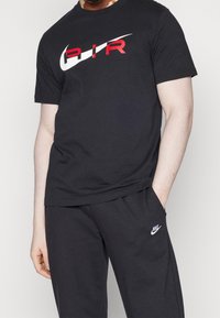 Svart bomullströja med en stor vit och röd "AIR" grafisk logotyp på framsidan. Ett par grå sweatsbyxor med en liten vit logotyp.