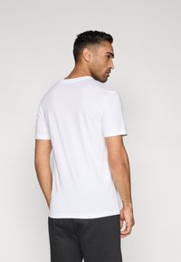 Λευκό T-shirt με κοντά μανίκια από βαμβάκι, με στρογγυλή λαιμόκοψη και άνετη εφαρμογή. Η πίσω όψη παρουσιάζει λεία υφή και καθαρές γραμμές.