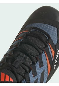 Czarne i niebieskie buty wspinaczkowe z pomarańczowymi akcentami, z teksturowaną siateczką na górze, sznurówkami oraz solidną ochroną gumową palców.