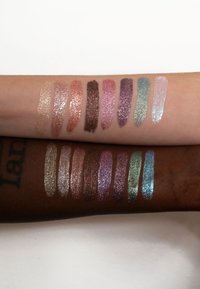 Due braccia mostrano campioni di glitter luccicanti in vari colori: oro, rosa, marrone, pink, lavanda, teal e blu. Inclusi diversi toni di pelle.