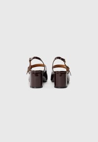 Brown patent leather block heel sandals with a back strap, adjustable buckle, and open toe, showcasing a smooth, glossy finish.