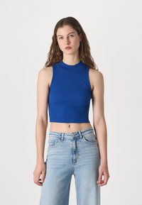 Sinine ribatud lühike topp kõrge kaelusega, kombineeritud heledate siniste denim laia jala teksadega. Sile tekstuur ja keha ligi jääv disain.